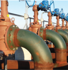 En serie av ventiler och rörsystem inom en industriell anläggning, med rostfärgad yta och blåa ventilmotorer.