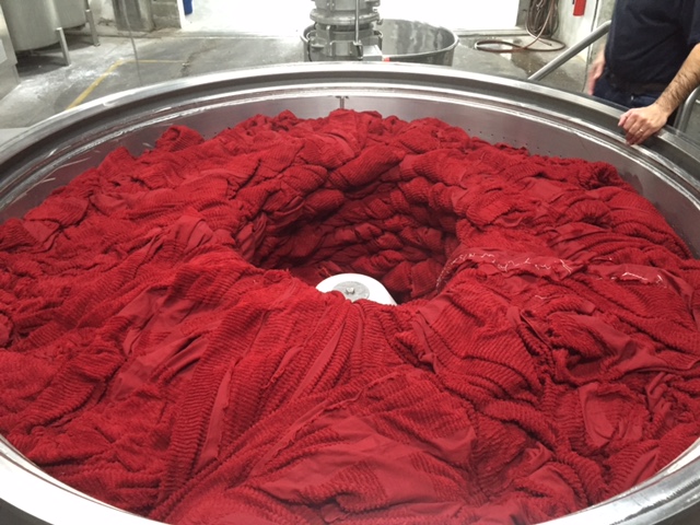 En stor, rund färgningsmaskin fylld med rödtextil, med en central del som visar en virvel av färgat material.
