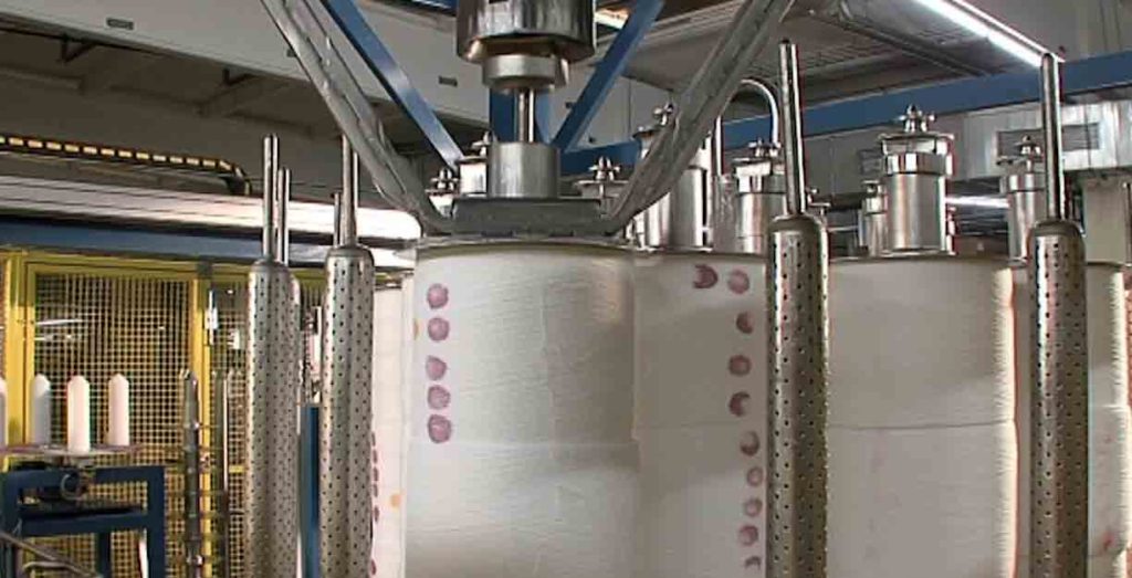 Kamera som visar automatiserat doseringssystem i en textilfabrik, med stora cylindrar för färg- och kemikaliehantering.