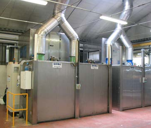 Två stora maskiner för textilhantering med metalliska ytor och avluftningsrör, placerade i en fabriksmiljö.