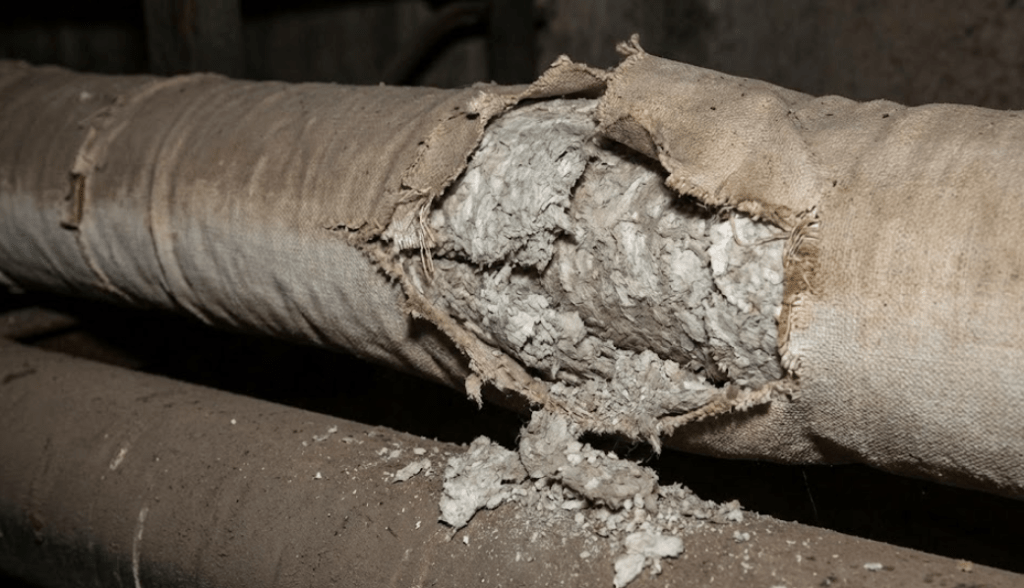 Bild som visar skadad rörisolering där det yttre höljet har brutits och exponerar ett ljust, fibrigt material inuti, vilket kan vara asbesthaltigt.